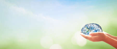 World mental health day concept. Human hands holding brain of earth over blurred nature background. Elements of this image furnished by NASAの写真素材