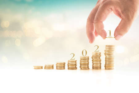 Human hand arrange 2021 letter on stack of coin