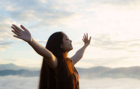 Worship God concept: Happy girl raised hand on blurred mountain sunrise background. Ai Yerweng, Bethong, Yala, Thailand, Asiaの写真素材