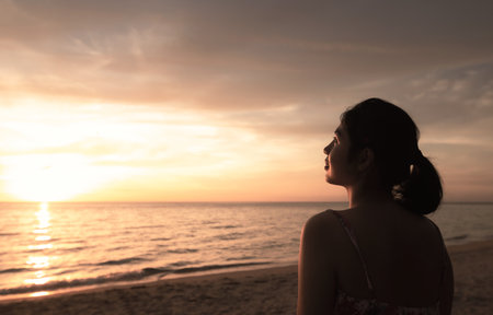 Worship God concept: Silhouette Asian woman raised hand on beach sunset backgroundの写真素材
