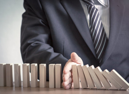 Management concept: Manager hand stopping the domino effect on office backgroundの写真素材