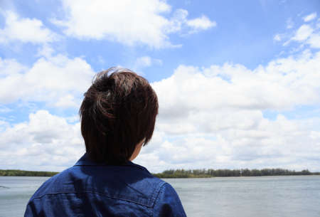 back of young man wear jeans shirt looking and thinking over blue sea sky backview