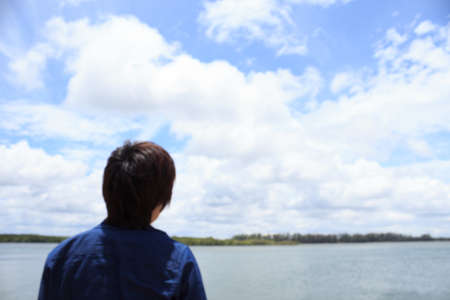back of young man wear jeans shirt looking and thinking over sea backviewの写真素材