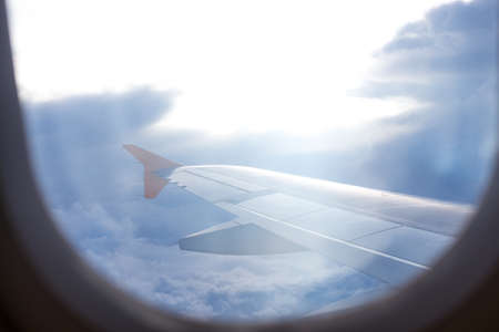 aerial view airplane wing and blue cloud sky, view through window glass above the clouds at sunsetの写真素材