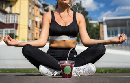 Woman sitting on the floor in lotus position with a glass of blueberry smoothie. Yoga and meditation, healthy eating.の写真素材