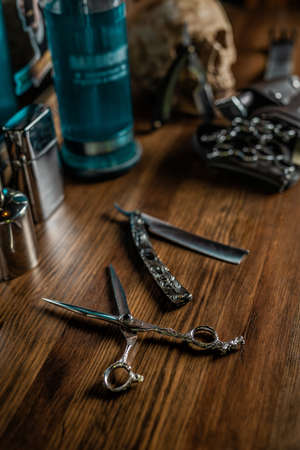 Hairdresser set of scissors, blades and other accessories on an old brown wooden table, with blurry backgroundの写真素材