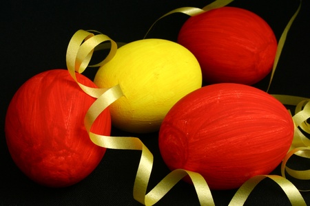 Three red and one yellow egg with a yellow ribbon on a black backgroundの写真素材