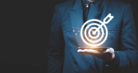 Businessman holding virtual dartboard and arrow with copy space for setup business objective target concept.の写真素材