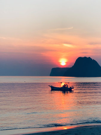 Orange Sky Serenity: A tranquil evening by the Thai coast, where a boat gracefully sails on the calm sea amidst a breathtaking sunset, casting a warm glow on the water and creating a picturesque sceneの写真素材