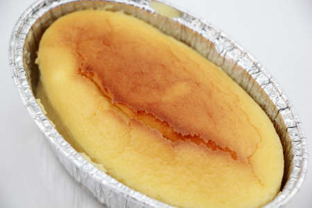 Close up of Golden brown plain cheese cake in oval disposable aluminum foil cup isolated on a white...