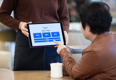 Senior Korean woman customer choosing the no-tip option on a tablet checkout screen presented by a restaurant server.