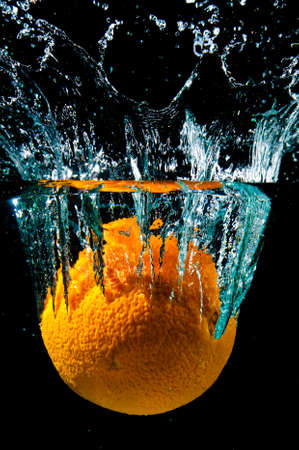 An orange in water with splash on black backgroundの写真素材