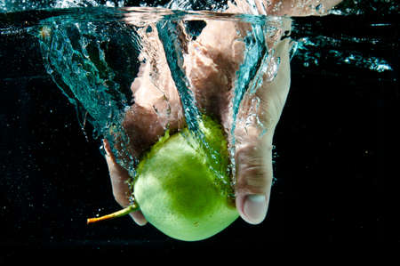 a hand holding pear in water with splash on black backgroundの写真素材