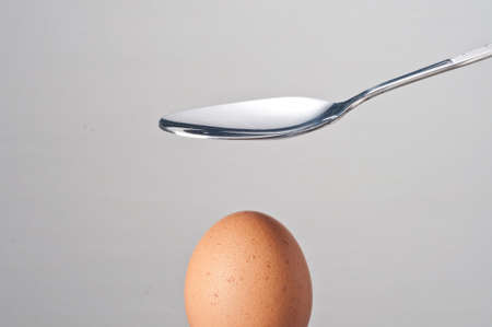 a metal spoon on an egg on gray background