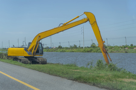 Yellow backhoe working riverside and on the roadsideの写真素材
