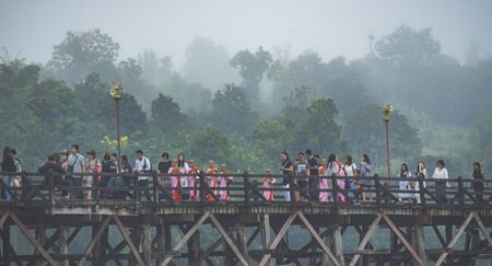 KANCHANABURI, THAILAND - APRIL 24: Buddhist monk walks on Auttamanusorn Wooden Bridge (Mon Bridge) with group of Mon students at Sangklaburi, Kanchanaburi, Thailand on November 24, 2016のeditorial素材