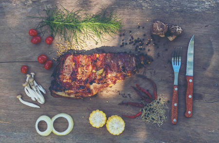 Spicy hot grilled spare ribs from a summer BBQ served with a hot chili pepper and fresh tomatoes on an old vintage wooden cutting boardの写真素材