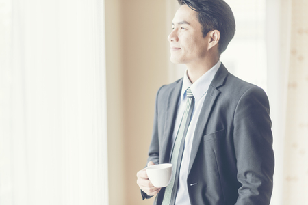 Half length portrait of a men dressed in luxury elegant clothes watching in window while standing in modern space, thoughtful successful businessman in suit resting after meeting with his partnersの写真素材