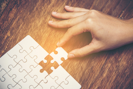 Close up of hand placing the last jigsaw puzzle piece, Hand holding missing jigsaw puzzle piece down in to the place, conceptual of problem solving, finding a solution.の写真素材