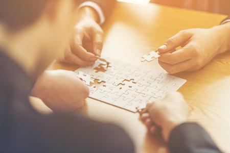 Businesspeople Hand Solving Jigsaw Puzzle On Wooden Desk, business conceptの写真素材