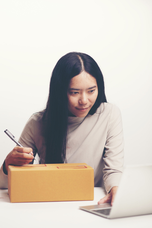 startup small business owner working with computer at workplace. freelance woman seller check product order, packing goods for delivery to customer. Online selling, e-commerce, shipping conceptの写真素材