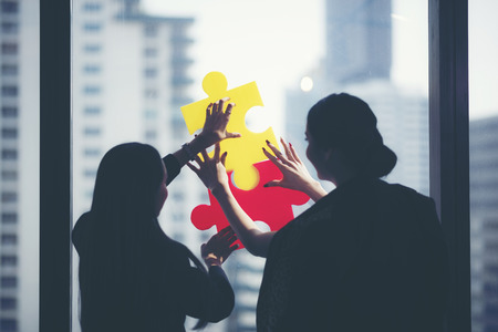 two businesswomen trying to connect couple puzzle piece with city sunset background, one part of whole. symbol of association and connection. business strategyの写真素材