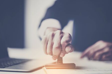 Close-up Of A Person's Hand Stamping With Approved Stamp On Document At Deskの写真素材