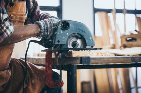 The carpenter is using an electric circular saw to cut the wood.