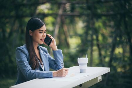 Asian business women are using smartphones to contact customers in the garden.の写真素材