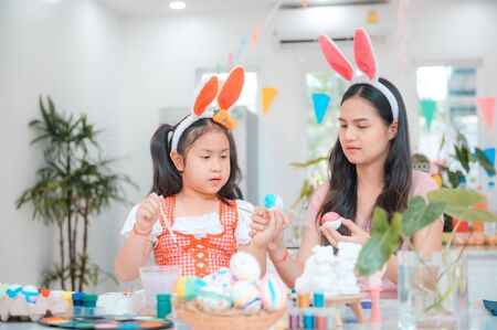 Attractive young woman with little cute girl are preparing for Easter celebration. Mom and daughter wearing bunny ears are having fun with Easter bunny while at home.の写真素材