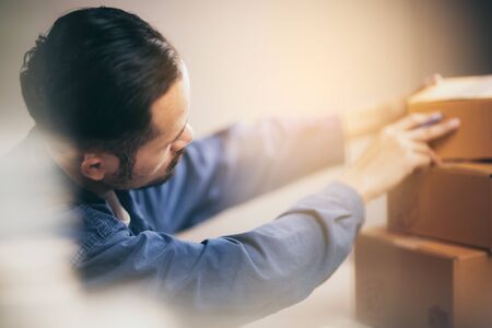 Young business start up online seller owner using laptop for checking the customer orders and preparing packages for productの写真素材