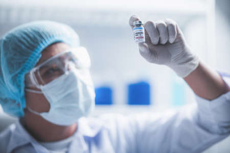 fight against COVID-19, coronavirus vaccine research in hospital laboratory, professional scientists holds bottle of new vaccine for virus cure treatment injection, medicine clinical during pandemicの写真素材
