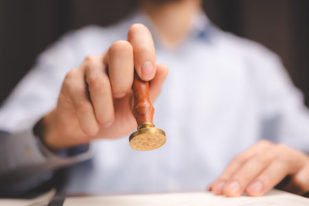Close-up of a person's hand stamping with approved stamp on certificate document public paper at desk, notary or business people work from home, isolated for coronavirus COVID-19 protectionの写真素材
