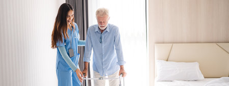 Portrait of Asian young nurse helping old elderly disable man grandfather to walk by using walker equipment in the bedroom. Senior patient of nursing home moving with walking frame and nurse supportの写真素材