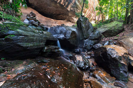 A beautiful forest waterfall and rocks between to the big cave.の写真素材