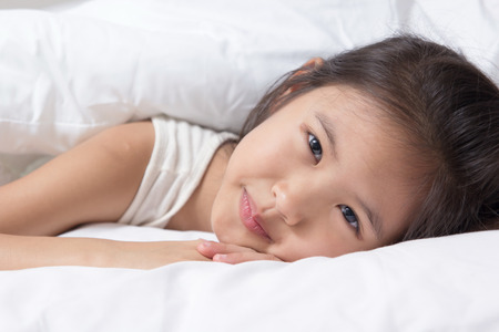 Adorable little Asian girl awaked up in her bedの写真素材