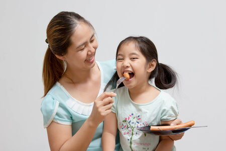 Asian mother feeding sausage to her daughterの写真素材