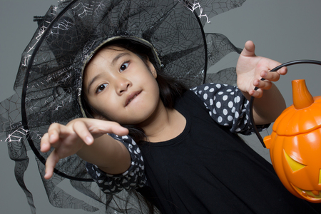 Portrait of little Asian girl in black hat and black clothing with pumpkinの写真素材