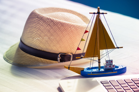 Vintage ship toy on the laptop and sun hat, travel concept.の写真素材
