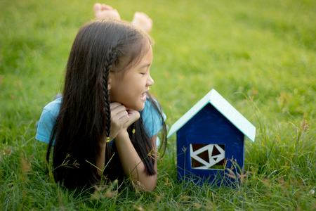 Little Asian child lying on the grass with house toyの写真素材