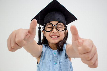 Happy Asian school kid graduate in graduation cap with big thumb upの写真素材