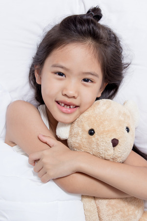 Adorable little Asian girl sleep on her bed with bear dollの写真素材