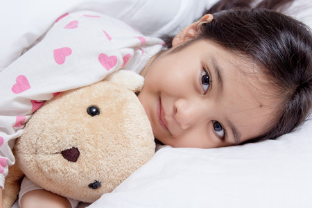 Adorable little Asian girl sleep on her bed with bear dollの写真素材