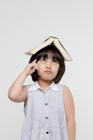 Portrait of little Asian child thinking and put a book on top with copy spaceの写真素材