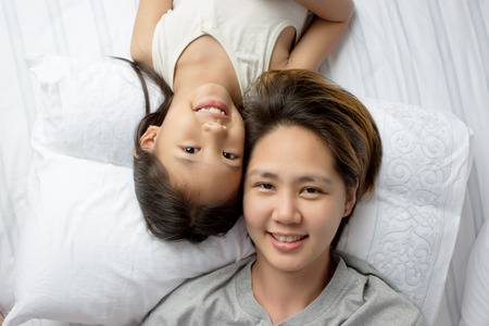 Portrait of happy Asian mother lying with daughter on the bedの写真素材