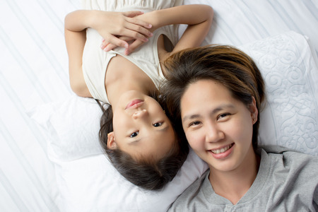 Portrait of happy Asian mother lying with daughter on the bedの写真素材