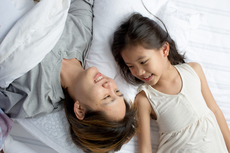 Portrait of happy Asian mother lying with daughter on the bedの写真素材