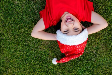 Little Asian girl in santa hat on the green grassの写真素材