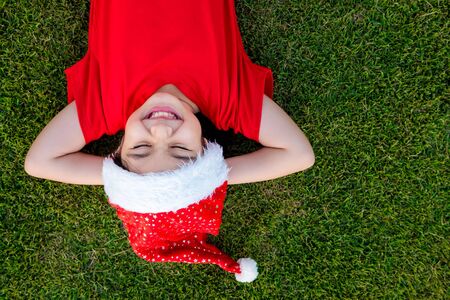 Little Asian girl in santa hat on the green grassの写真素材