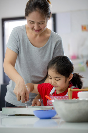 Little Asian cute chef cooking a bakery in kitchen with motherの写真素材
